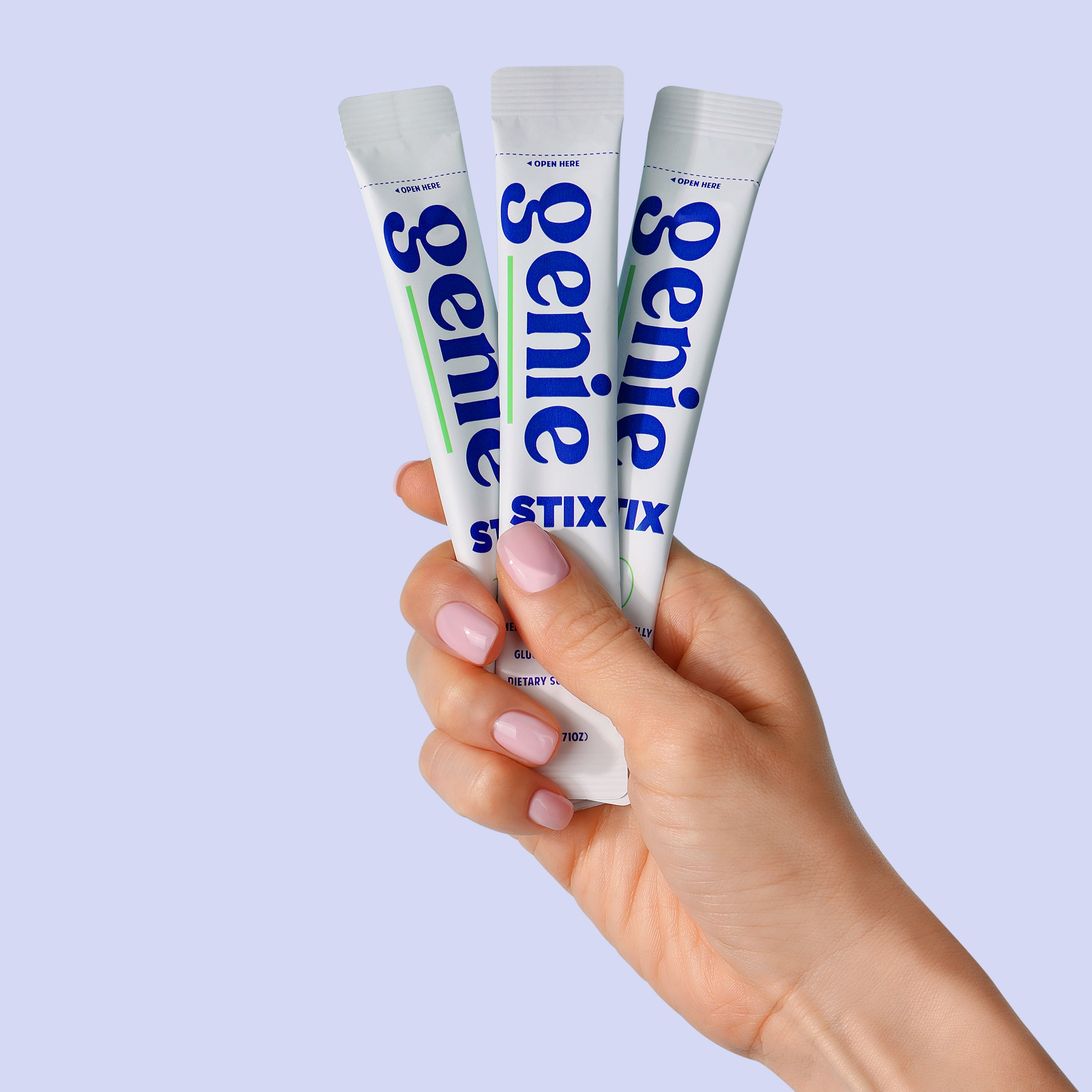 Hand holding three 'Genie Stix' products against a light purple background